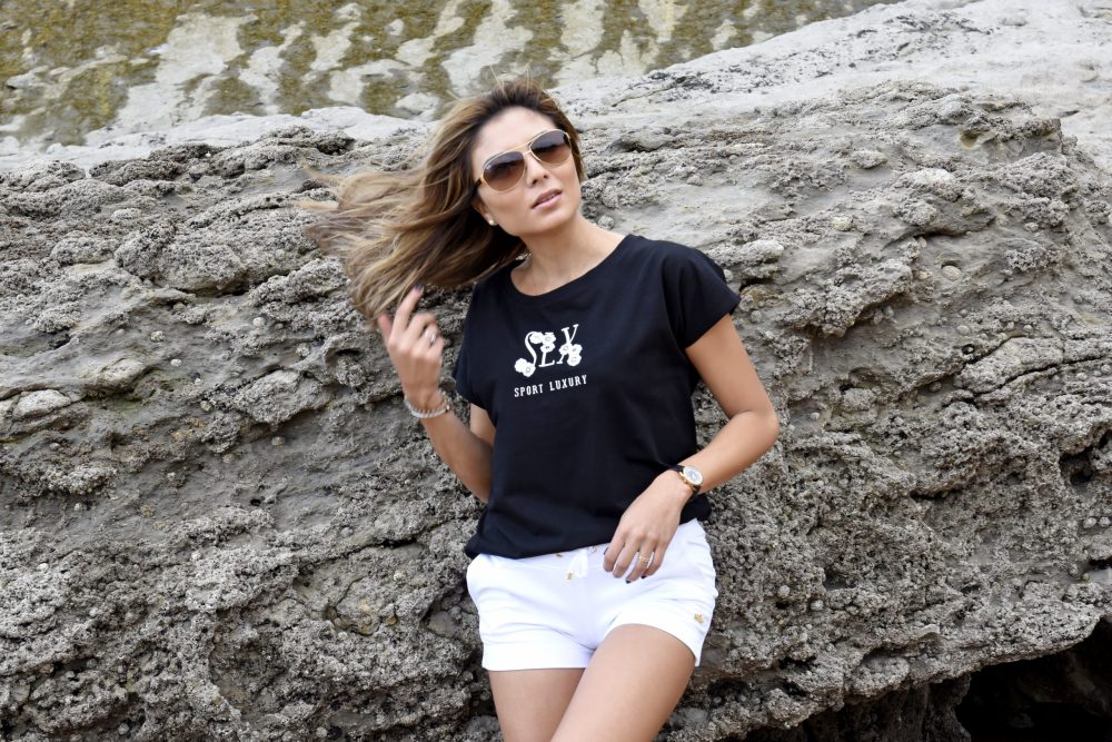 mujer apoyada en una roca con un short blanco y una camiseta negra