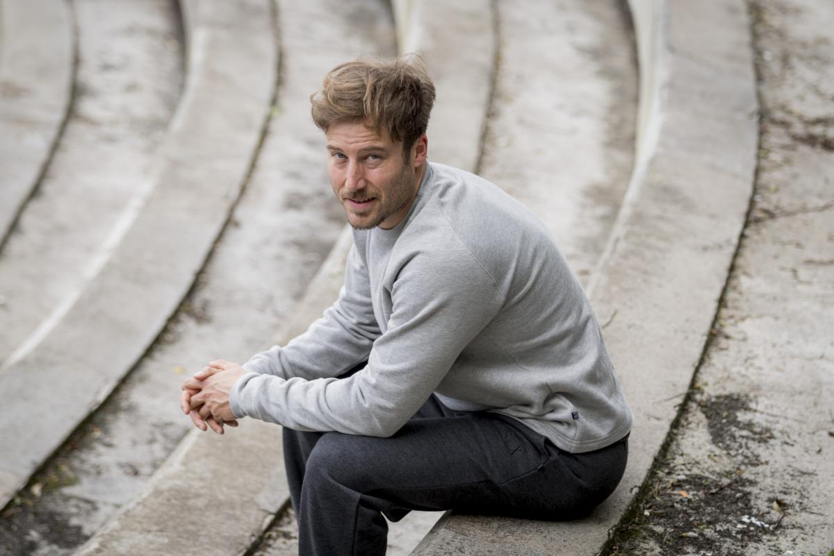 HOMBRE SENTADO EN UN ESCALON CON SUADERA GRIS CLARA Y PANTALON GRIS OSCURO