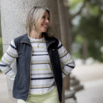 chica apoyada en una columna con una chaqueta lisas marino con mangas a rayas de colores y camiseta a conjunto.