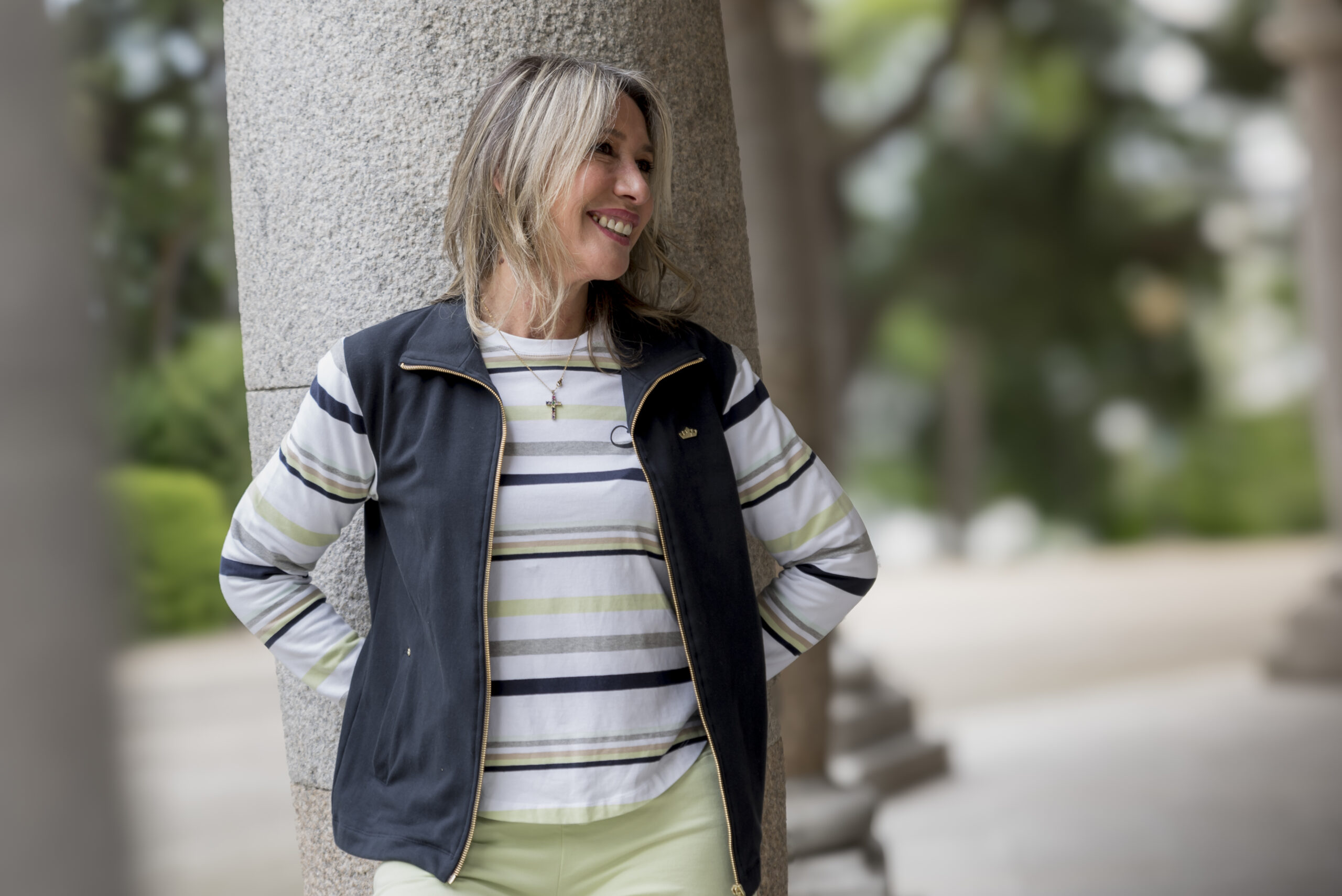 chica apoyada en una columna con una chaqueta lisas marino con mangas a rayas de colores y camiseta a conjunto.