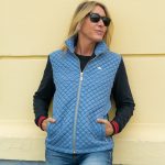 una mujer aployada en una pared amarilla con una chaqueta acolchada celeste con las mangas marinas.