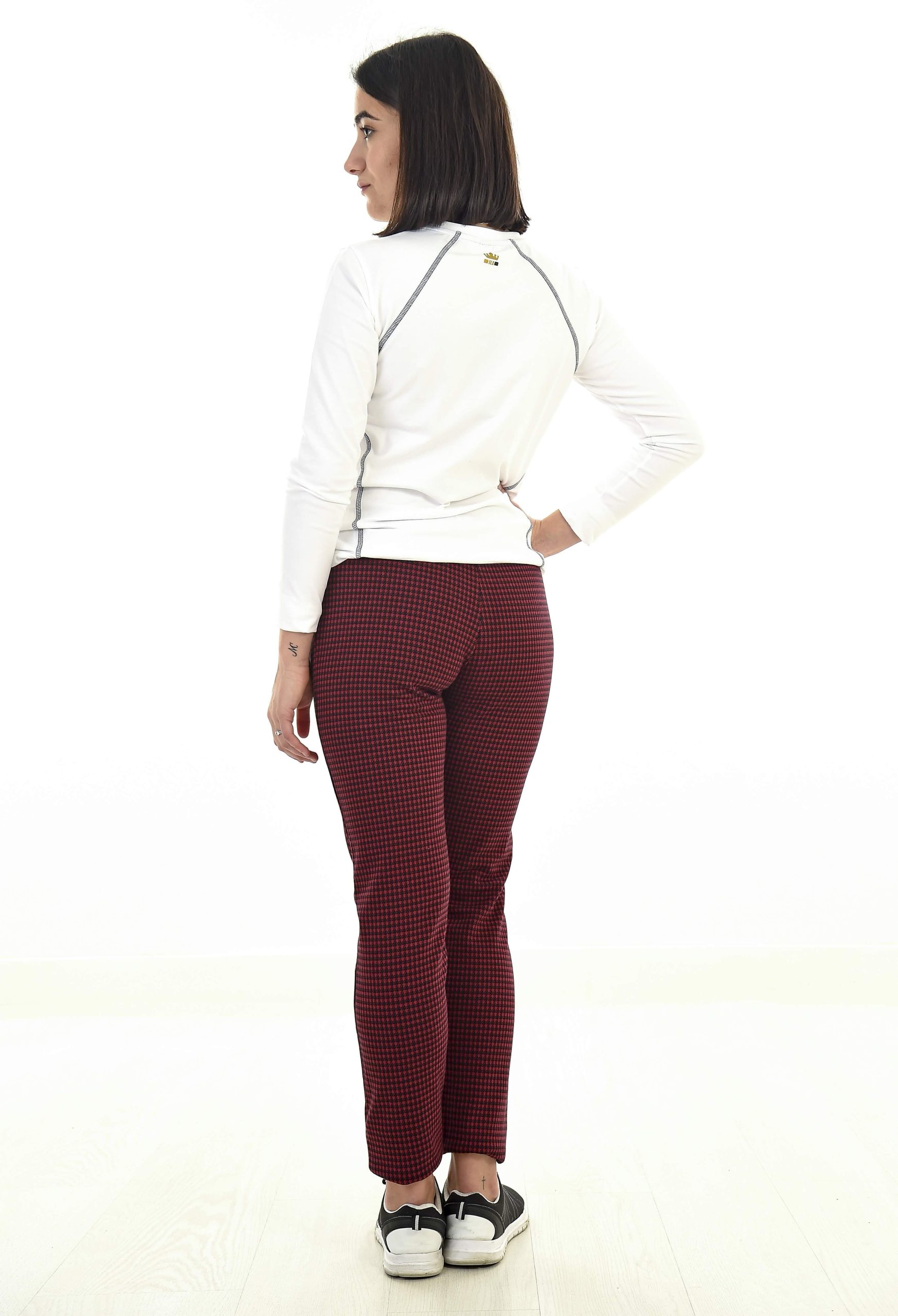 MUJER EN FONDO BLANCO CON UN PANTALON DE CUADROS NEGRO Y ROJO Y UN POLAR BLANCO CON PESPUNTES NEGROS DE ESPALDA