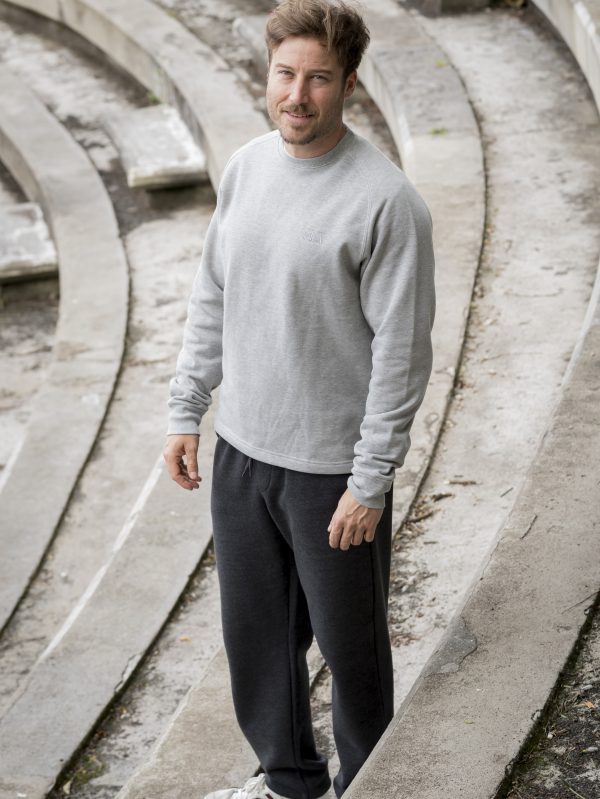 HOMNRE DE PIES EN UNAS GRADAS DE CEMENTO CON UN PANTALON GRIS MARENGO Y UNA SUDADERA GRIS MEZCLA