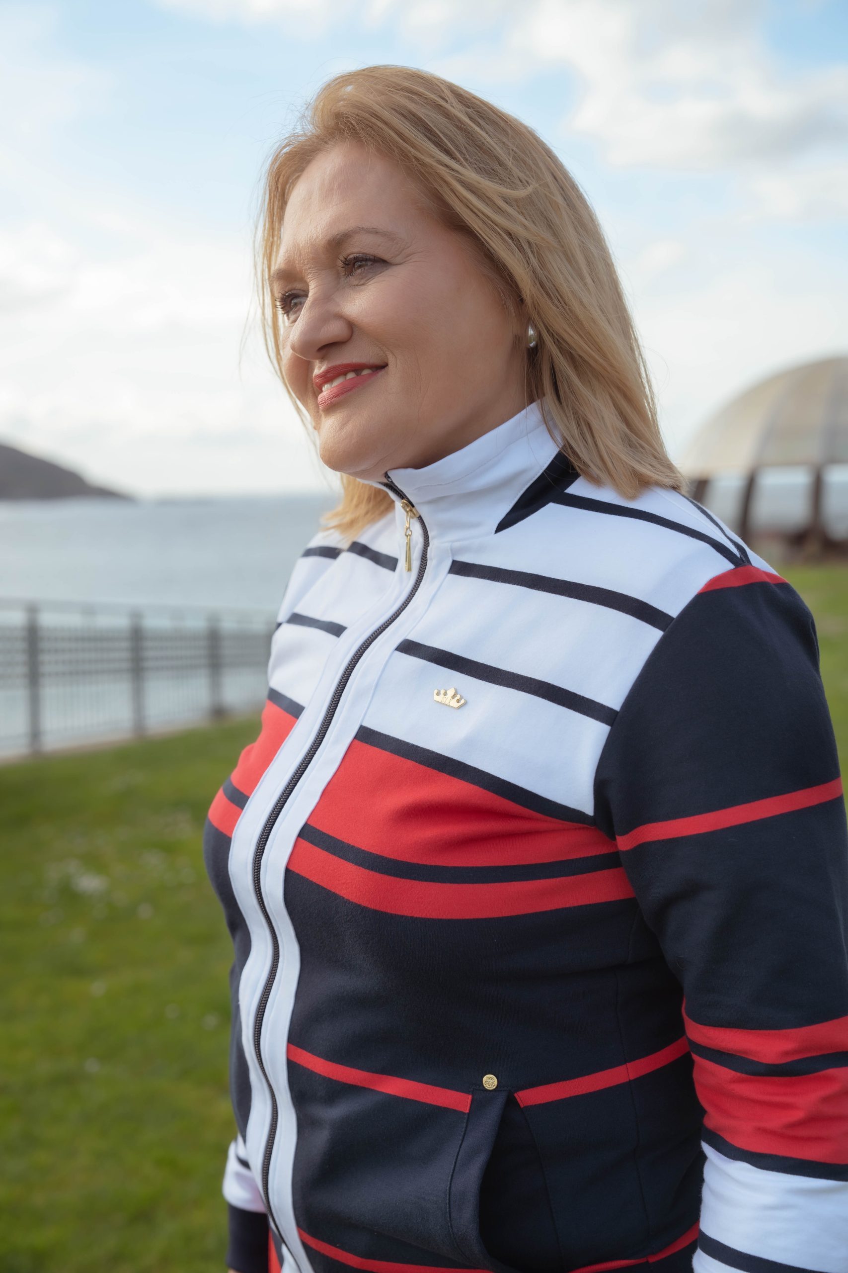 MUJER MIRANDO AL HORIZONTE EN UN CESPES CON UNA CHAQUETA MARINERA EN COLOR BLANCA, ROJA Y MARINO.