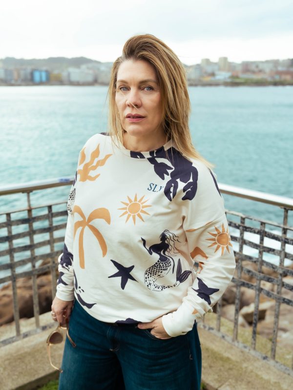 chica en una barandilla con el mar de fondo y nuestra sudadera sirena con un estampado super veraniego