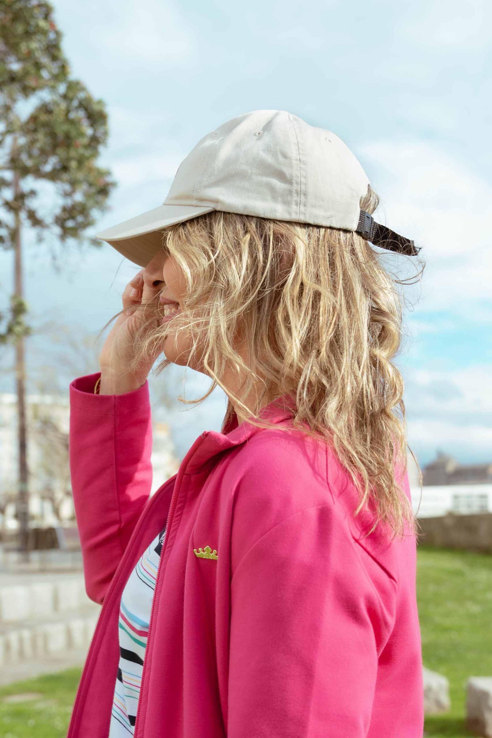 MUJER MIRANDO A LO LO LEJOS CON UNA GORRA BEIGE, PELO RUBIO Y UNA CHAQUETA EN COLOR ROSA FUCSIA