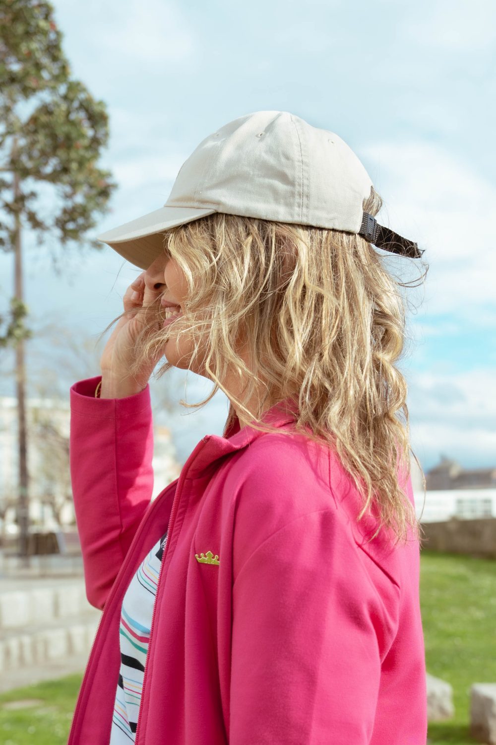 MUJER MIRANDO A LO LO LEJOS CON UNA GORRA BEIGE, PELO RUBIO Y UNA CHAQUETA EN COLOR ROSA FUCSIA