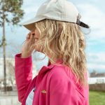 MUJER MIRANDO A LO LO LEJOS CON UNA GORRA BEIGE, PELO RUBIO Y UNA CHAQUETA EN COLOR ROSA FUCSIA