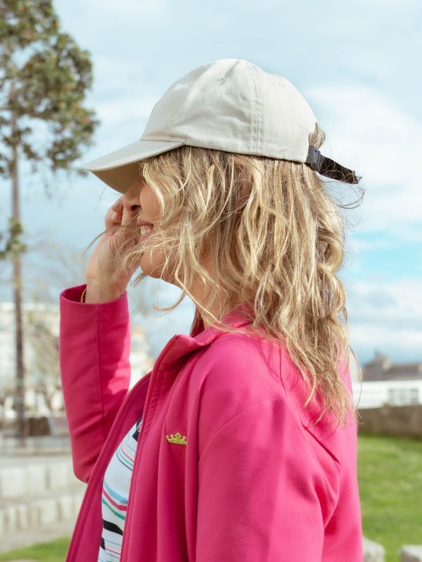 MUJER MIRANDO A LO LO LEJOS CON UNA GORRA BEIGE, PELO RUBIO Y UNA CHAQUETA EN COLOR ROSA FUCSIA